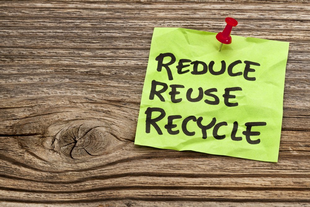 Sticky note saying reduce reuse recycle pinned to wooden board