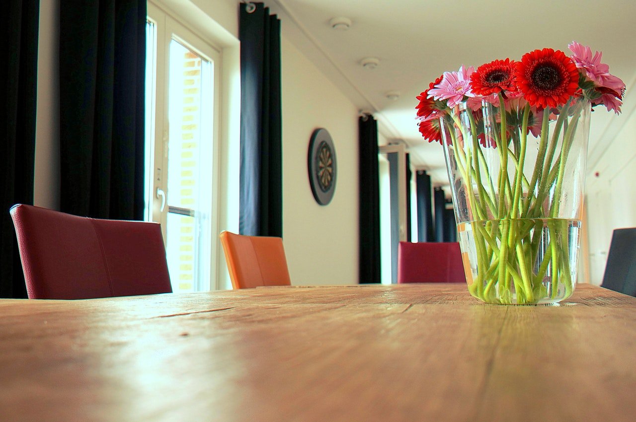 A vase of flowers on a wooden table in a large bright room.