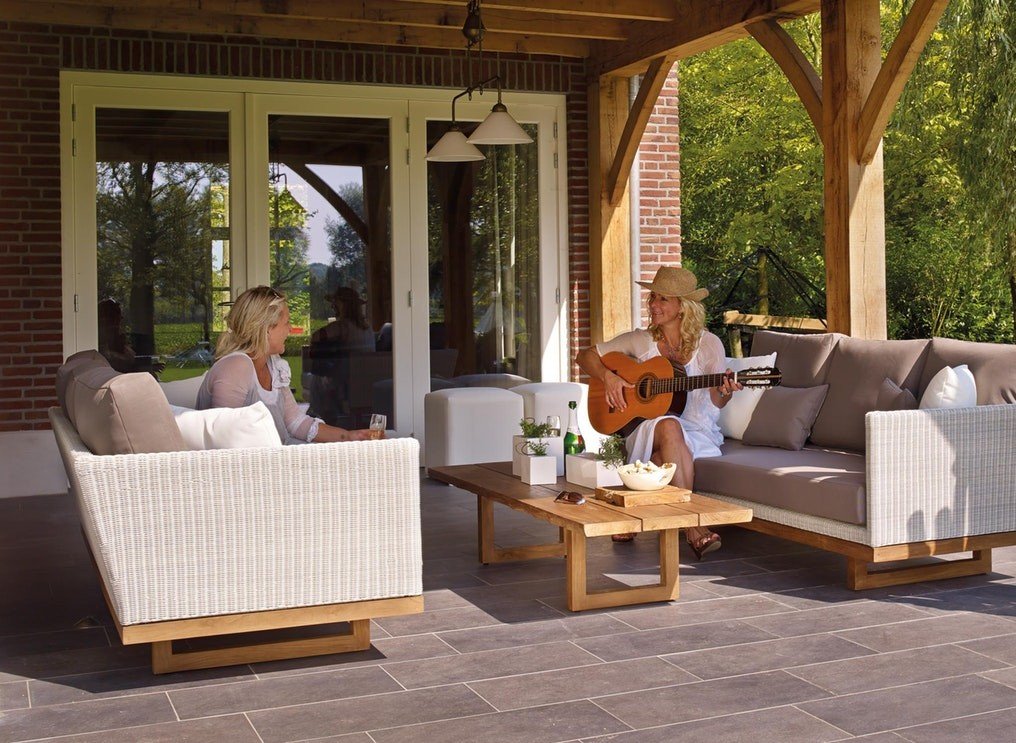 A large patio area with porch. Seating and table. Two ladies with snacks and drinks chatting, one playing guitar.