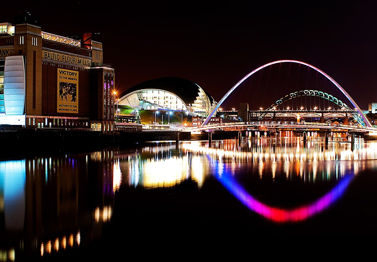 A photo of Newcastle at night. Colourful lights illuminate the river Tyne