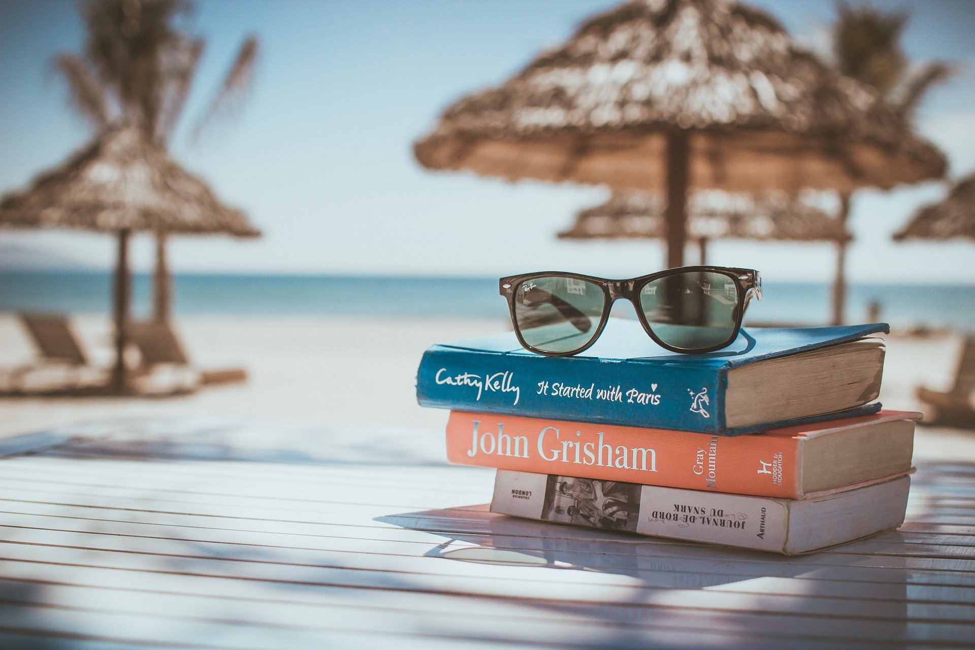 A pile of books, sunglasses on top, on table next to beach