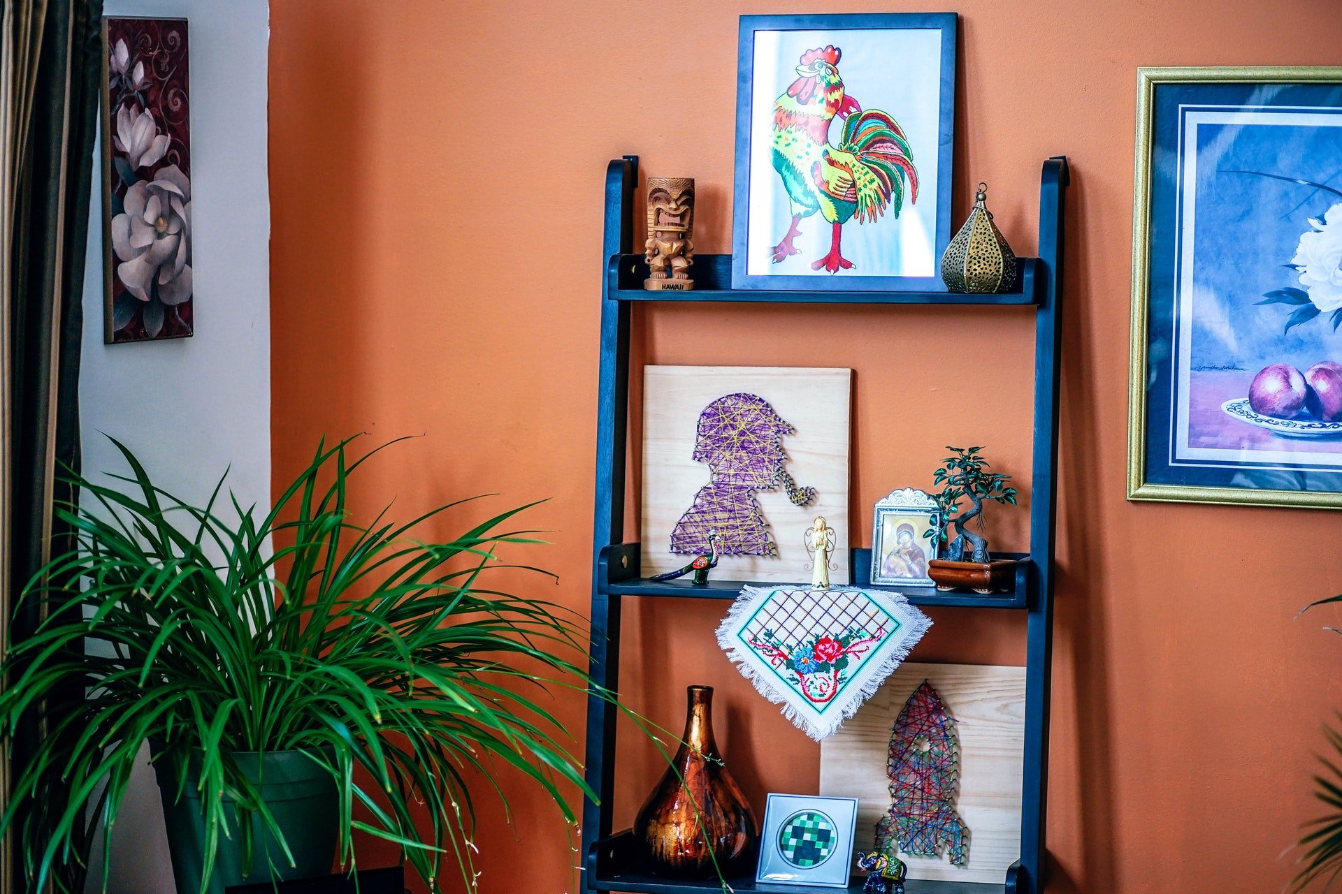 A shelf full of artwork with a green plant in the corner of the room