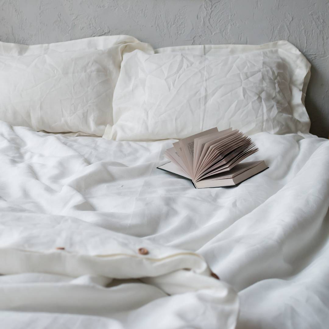 A very comfortable looking bed with a thick, ruffled white comforter. A book is resting near the pillows.