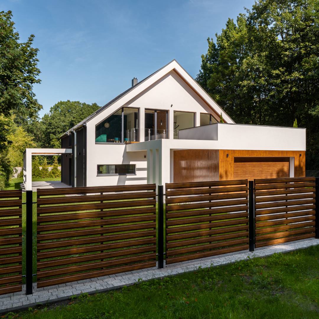 A modern white house features exterior wood paneling and a horizontal fence with minimal visibility, built using metal posts.