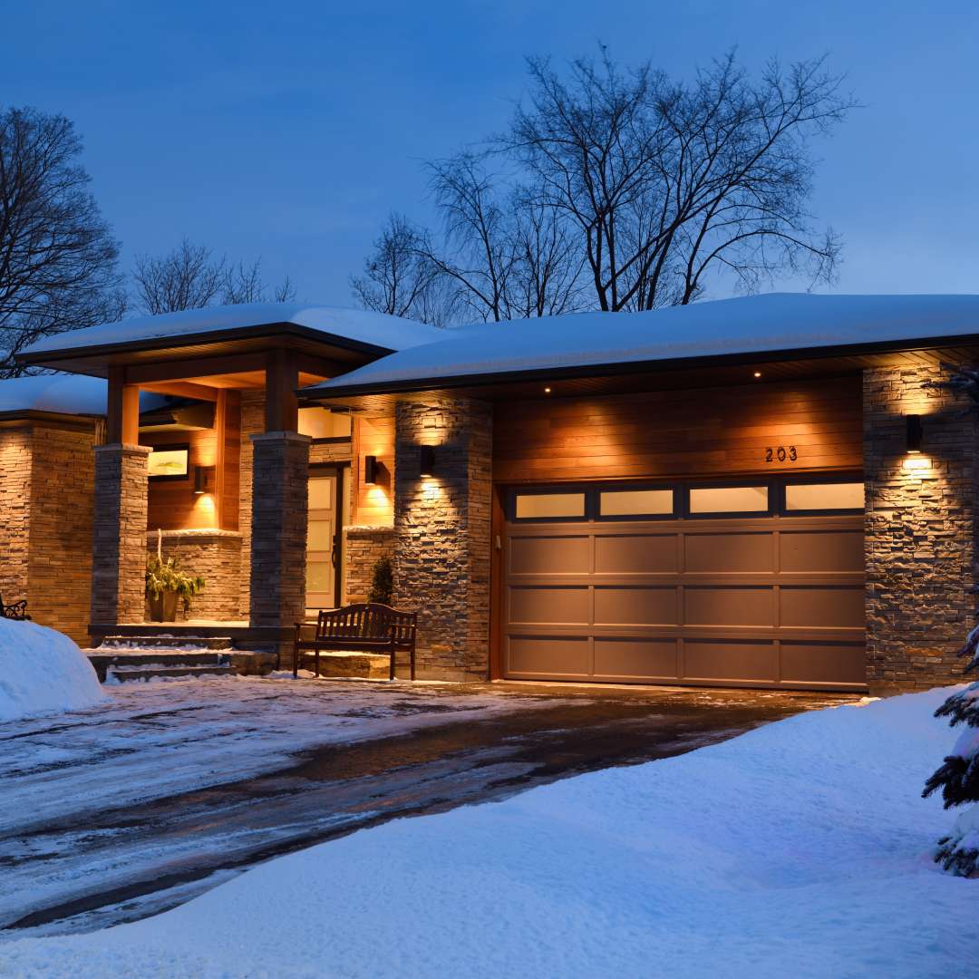 The exterior of a modern house during winter is covered in snow. The driveway was plowed in front of the two-car garage.