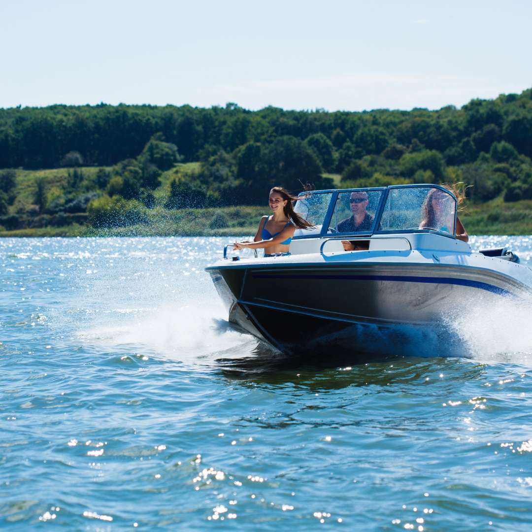 A speed boat on the lake with three passengers inside. The sun is shining and the water is relatively calm.