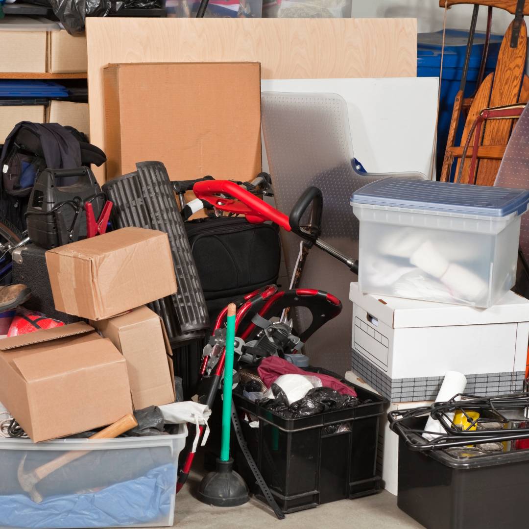 A very messy garage full of boxes, bag, and various stored items. Some of the items include old shoes and sports gear.