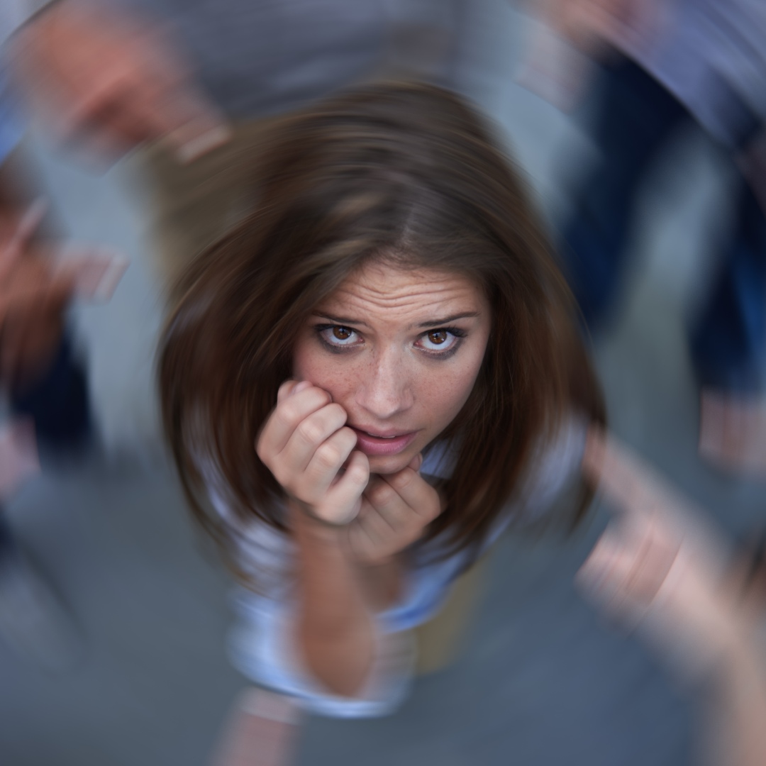 A top view of a young woman with an anxious expression and hands to her face. Her surroundings are blurred in a swirl.