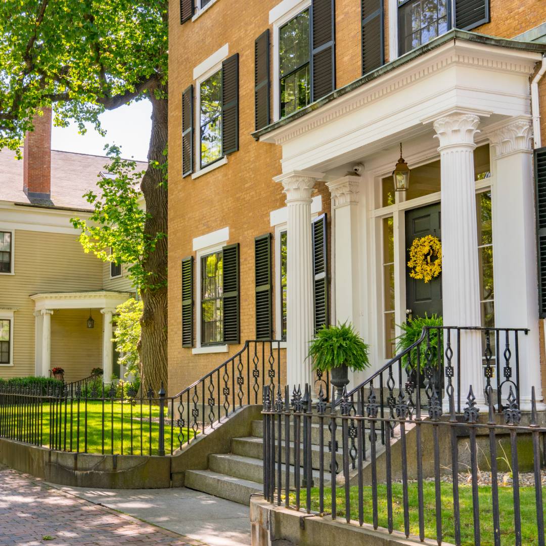 A row of early American-style historic homes lining a residential street. Each boasts colorful siding and brick exteriors.