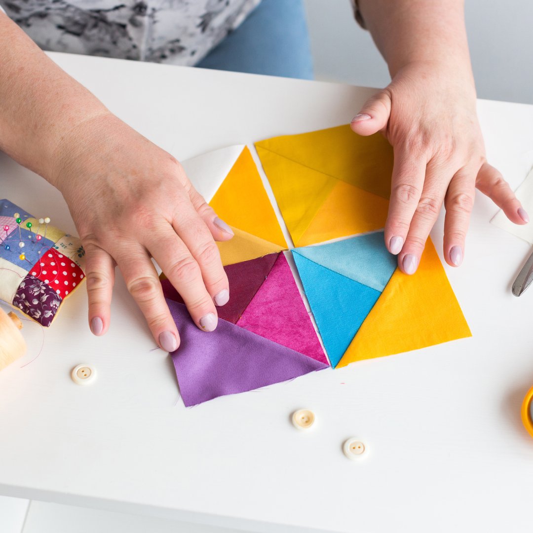 A hobbyist quilter at their sewing table with a selection of pre-cut fabric shapes. They also have scissors nearby.