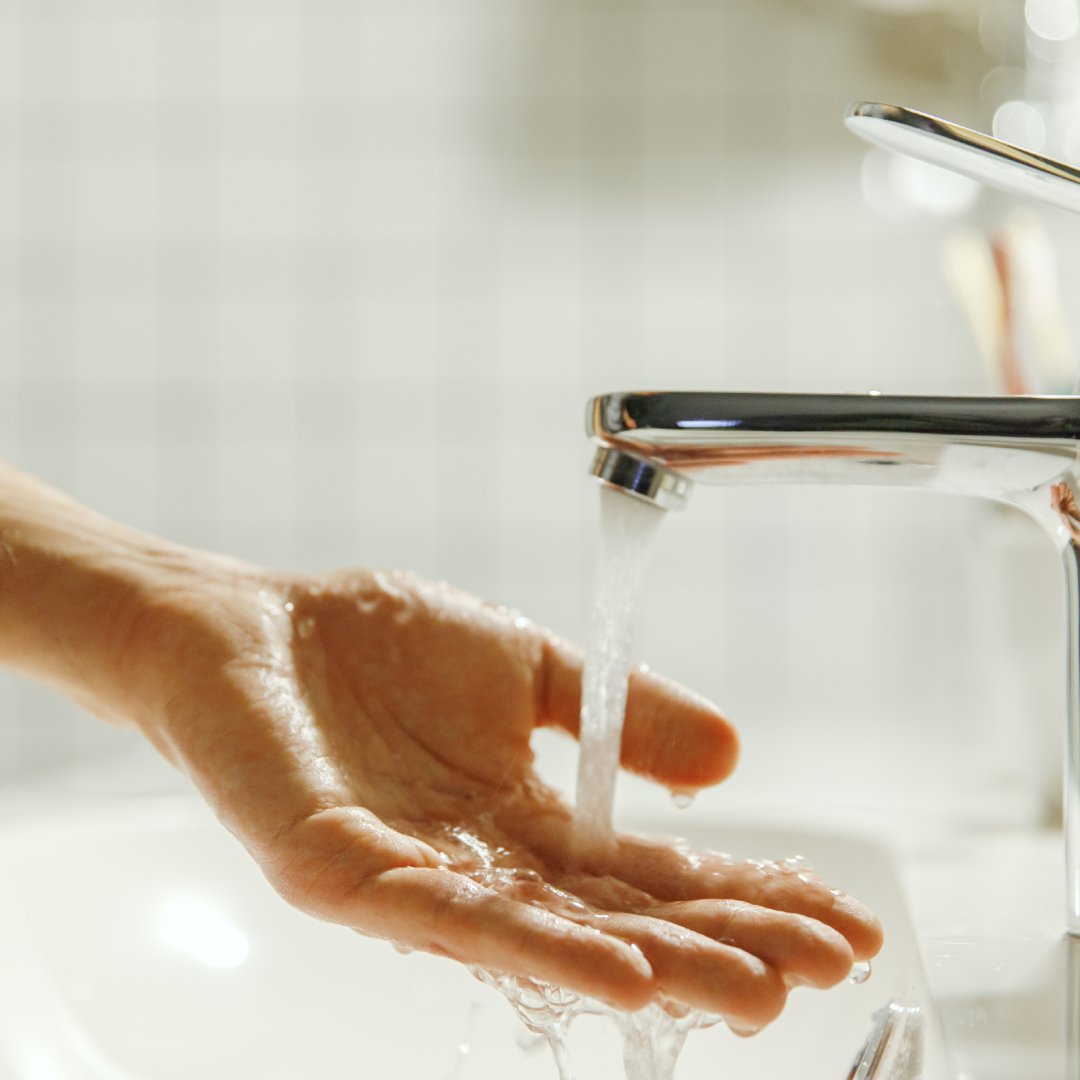 A person reaching out and holding their hand beneath a running faucet. The water cascades onto their hand.