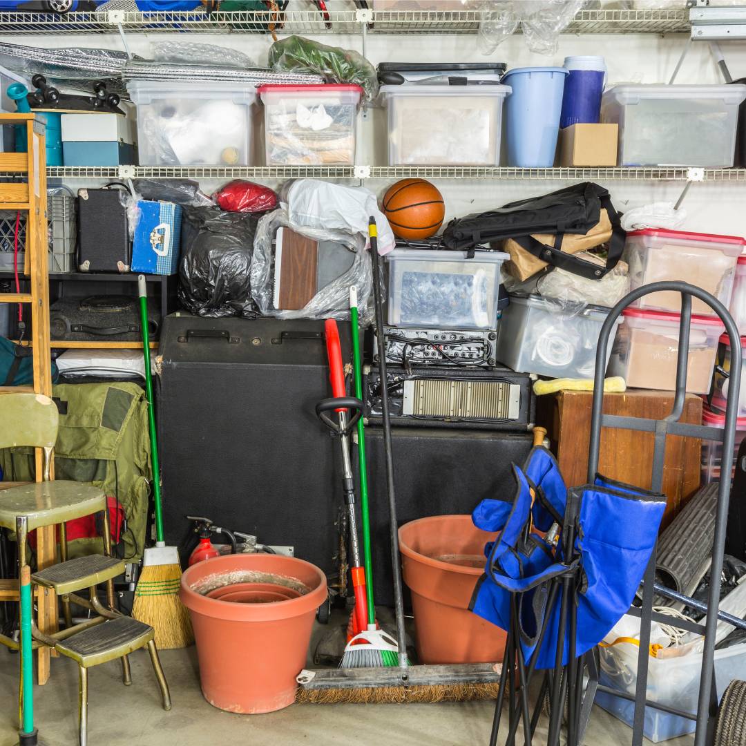 The interior of a very cluttered garage. Strewn about are tools, storage bins, cleaning supplies, and recreational gear.