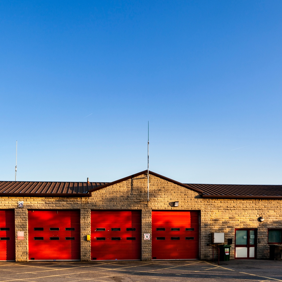 A community firestation with four large, red garage doors and a small entrance on the right side next to windows.