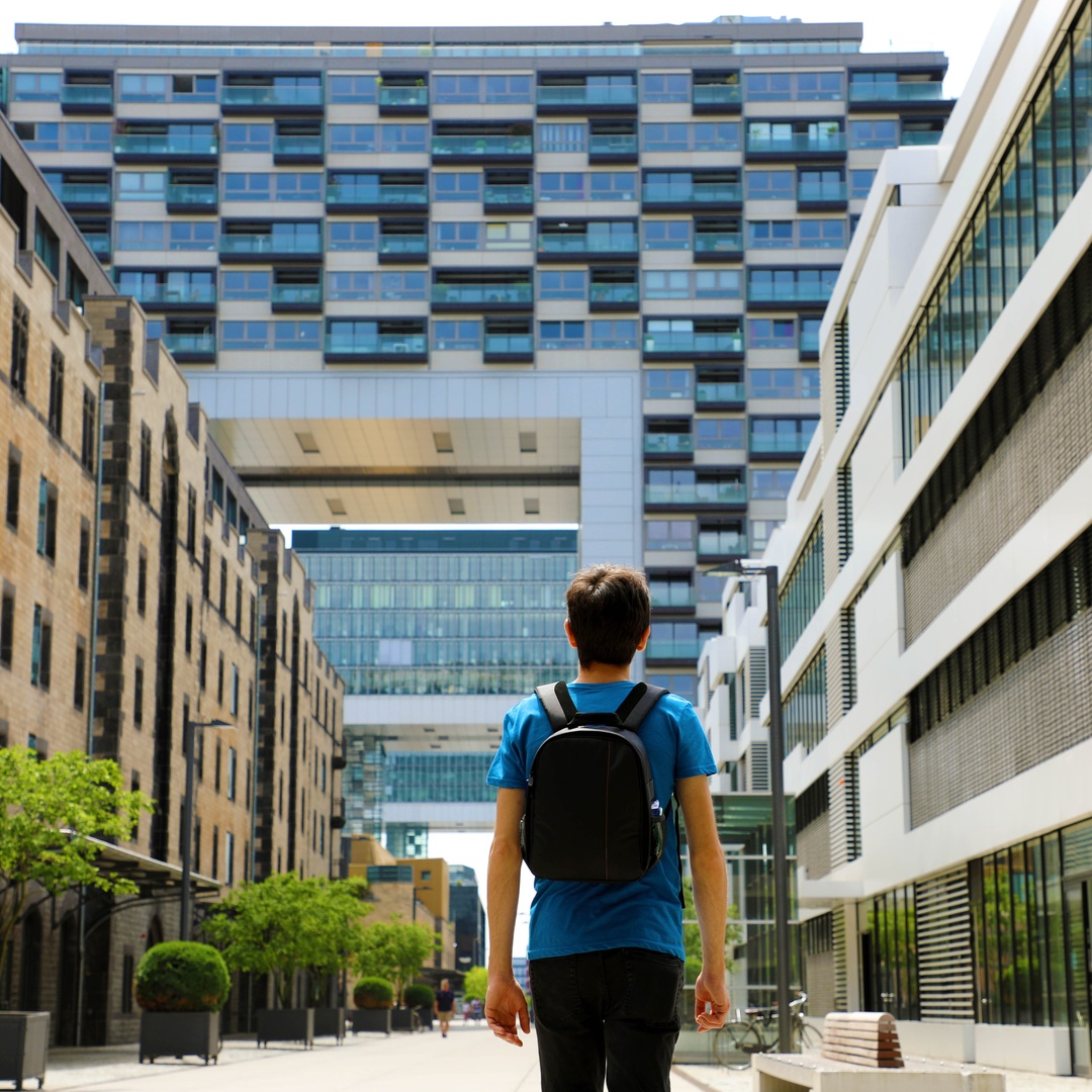 Rear view of a young man wearing a backpack as he looks at the buildings in a large city in front of him.