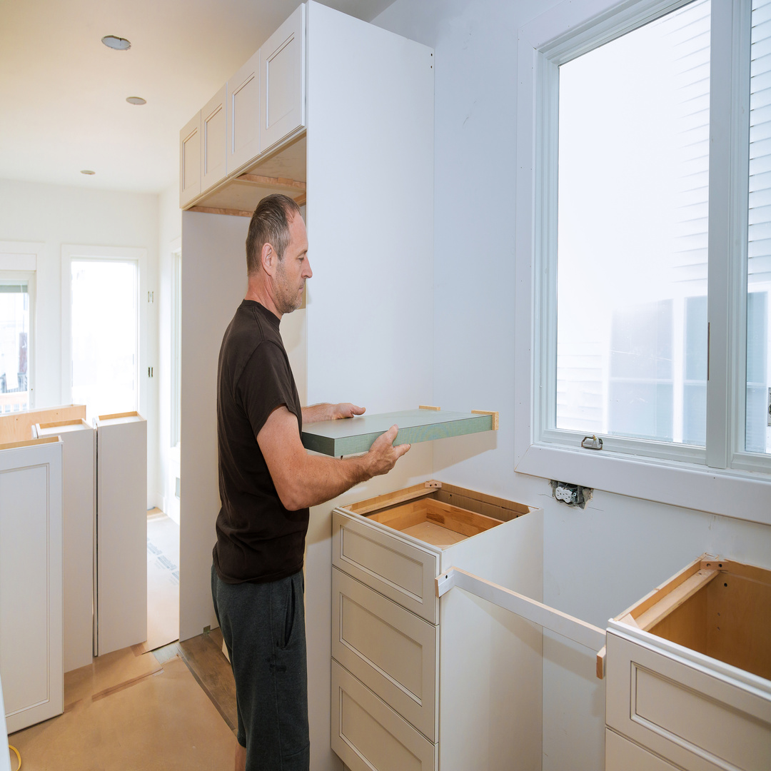 A contractor wearing a black shirt installing a countertop inside a large residential kitchen during the daytime.