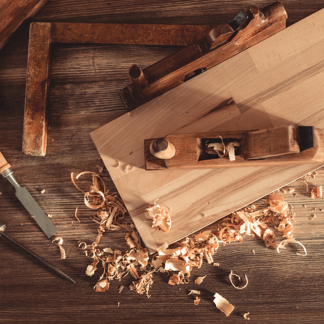 A wooden work surface with various woodworking tools and a wooden board on the top with wood shavings scattered.