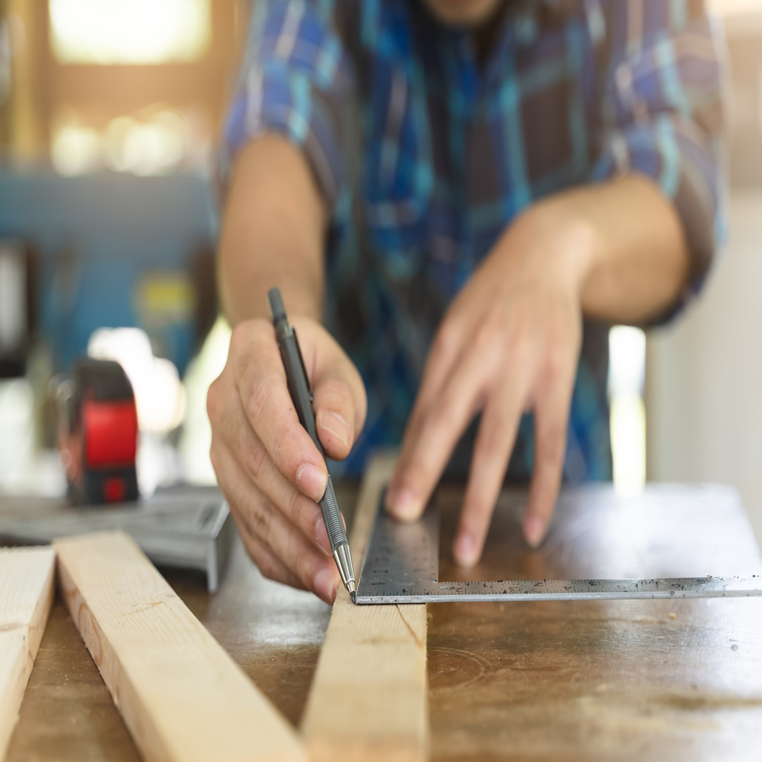Close-up of a person's hands as he works on a DIY project. The person measures wood and makes marks with a pen.