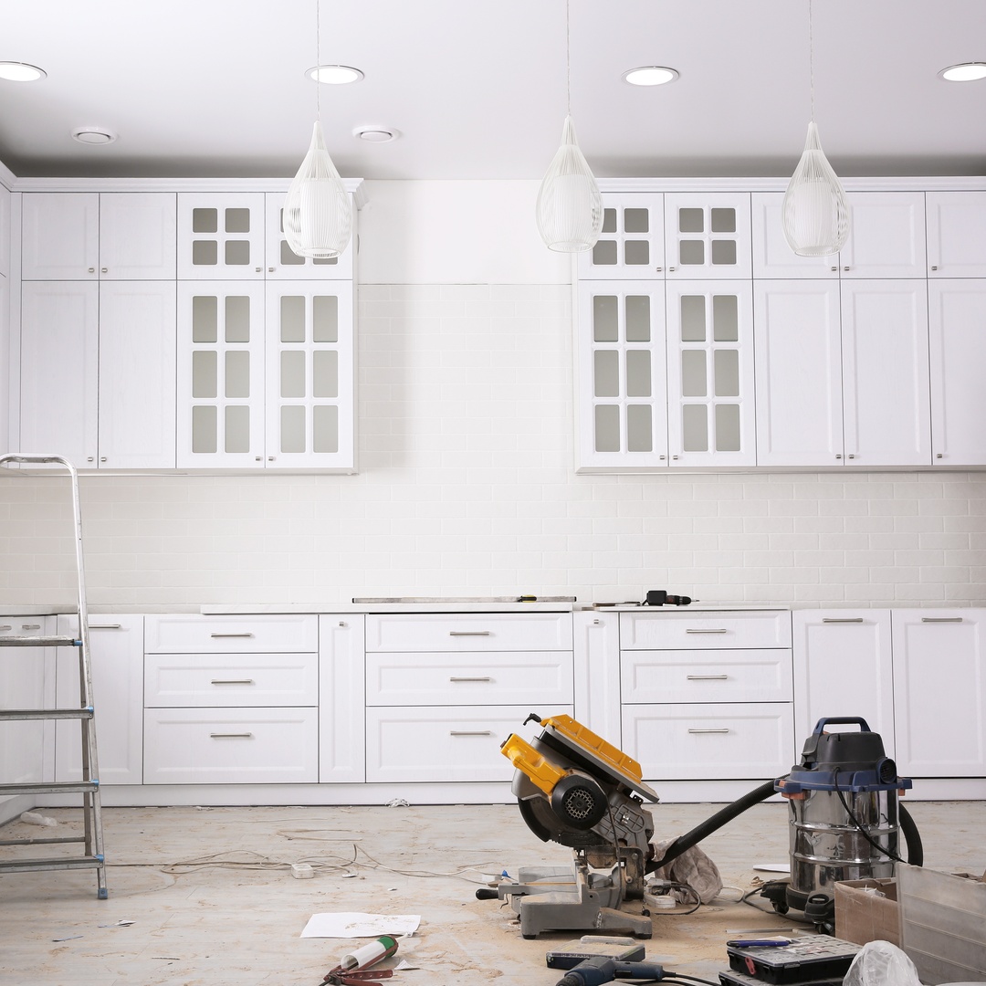 A kitchen in the process of being remodeled, with tools on the floor. The cabinets and drawers are white with silver handles.